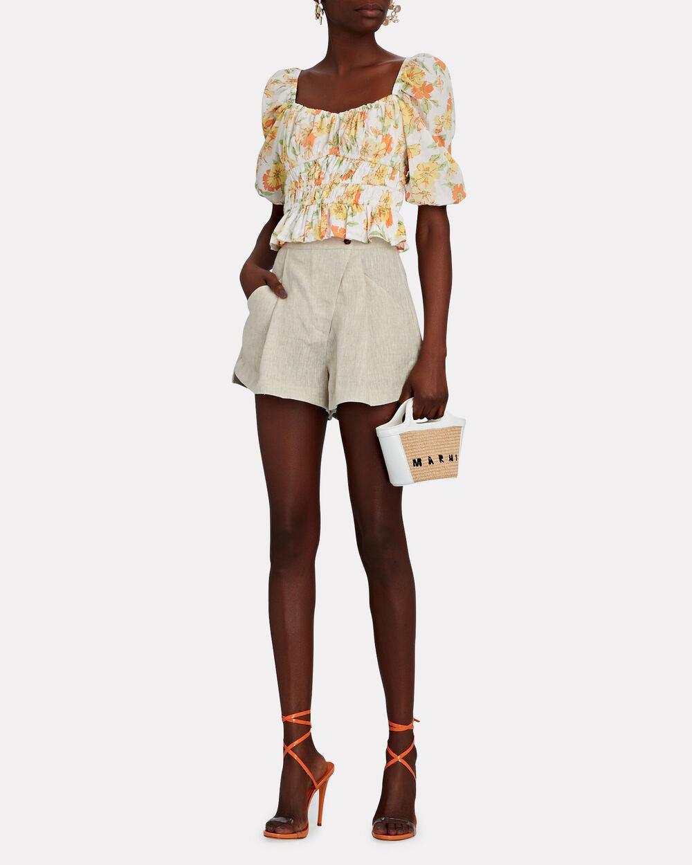 Kvinne med blomstrete topp, beige linshorts, oransje sandaler og liten veske.