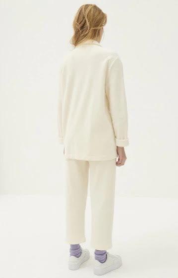 Kvinne med lyst hår iført kremfarget blazer og bukse i minimalistisk studio.