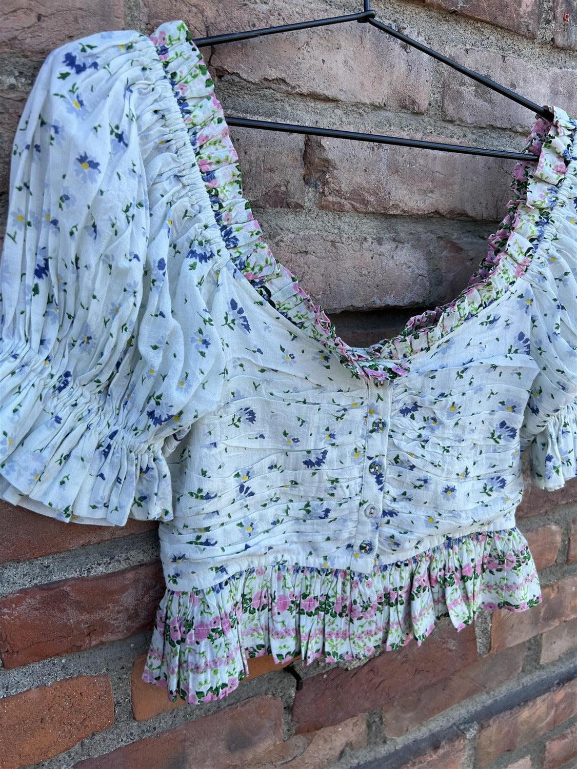 Bohemsk topp med blå blomster, korte puffermer og volang, henger på murvegg.