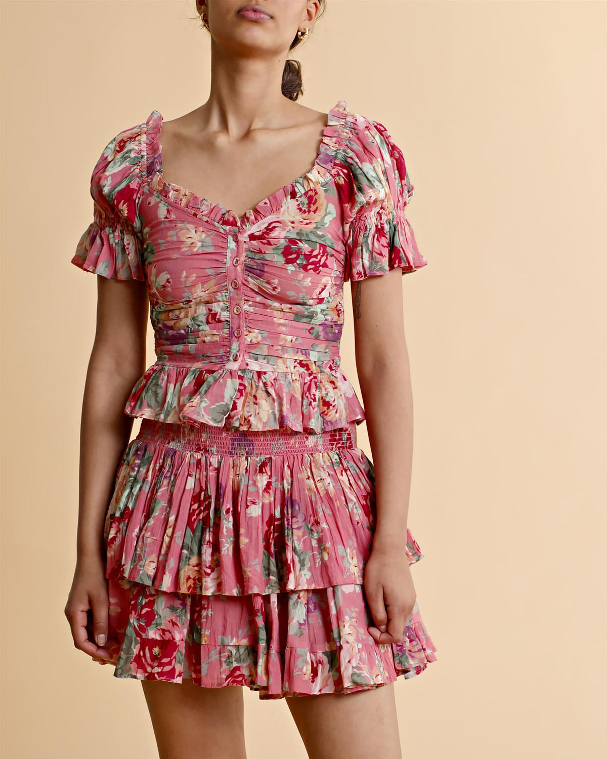Dame i bohemsk rosa bluse og skjørt med blomsterprint og volanger mot beige bakgrunn