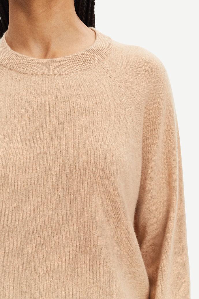 Beige damegenser i ull med rund hals, vises fra bryst til hals mot lys bakgrunn