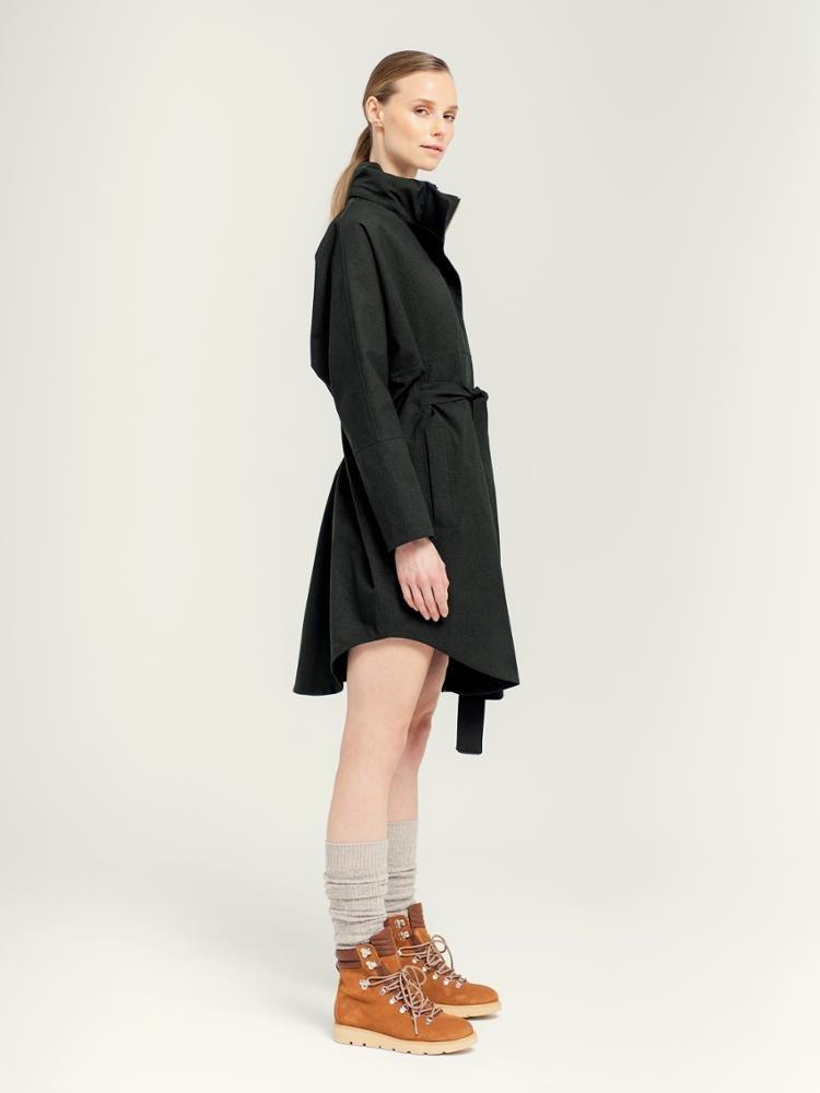 Dame i sort poncho med belte, beige ullsokker og brune sko mot lys bakgrunn