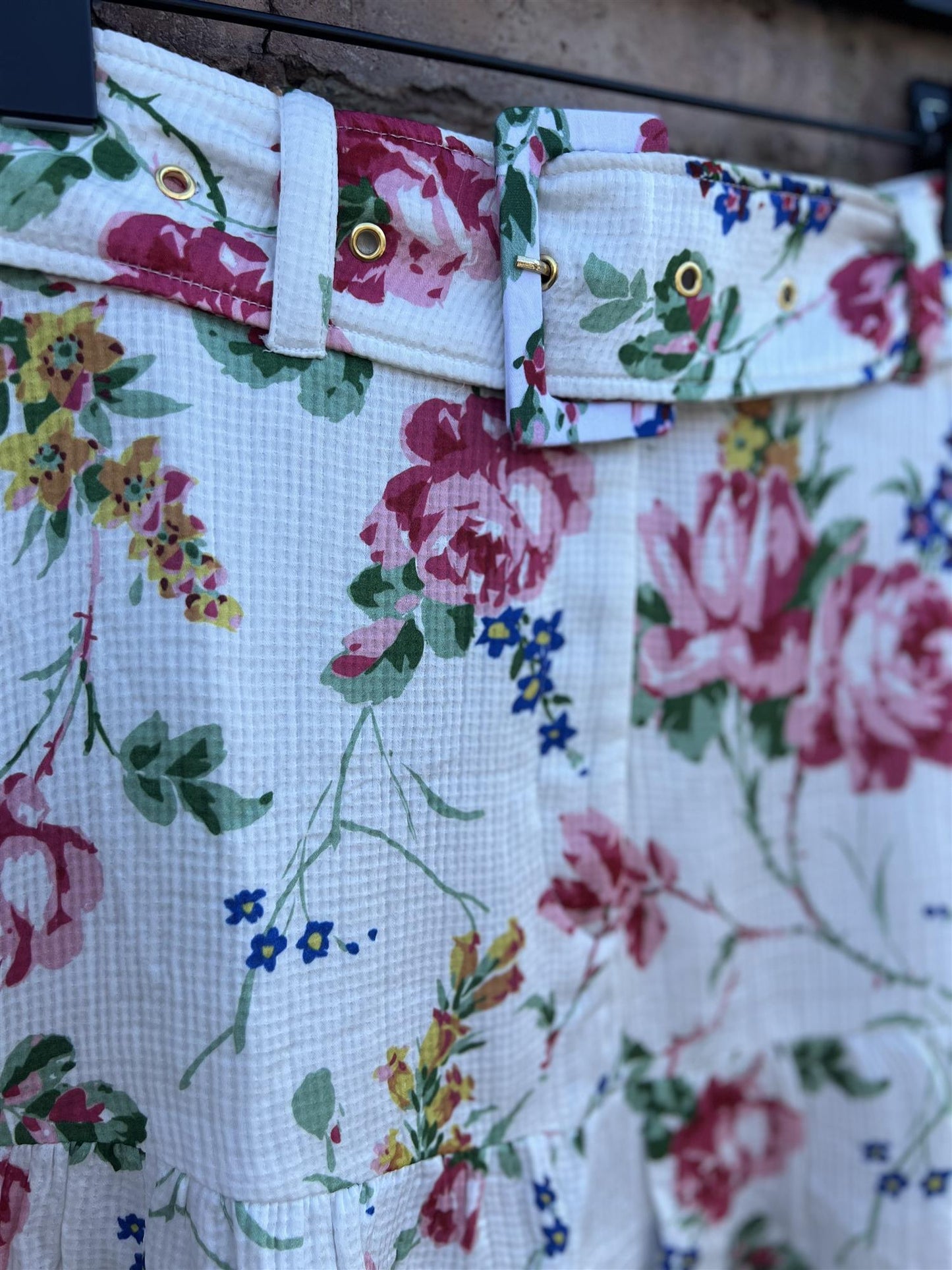 Nærbilde av hvit sateng skjørt med fargerikt blomsterprint og belte med gullmaljer