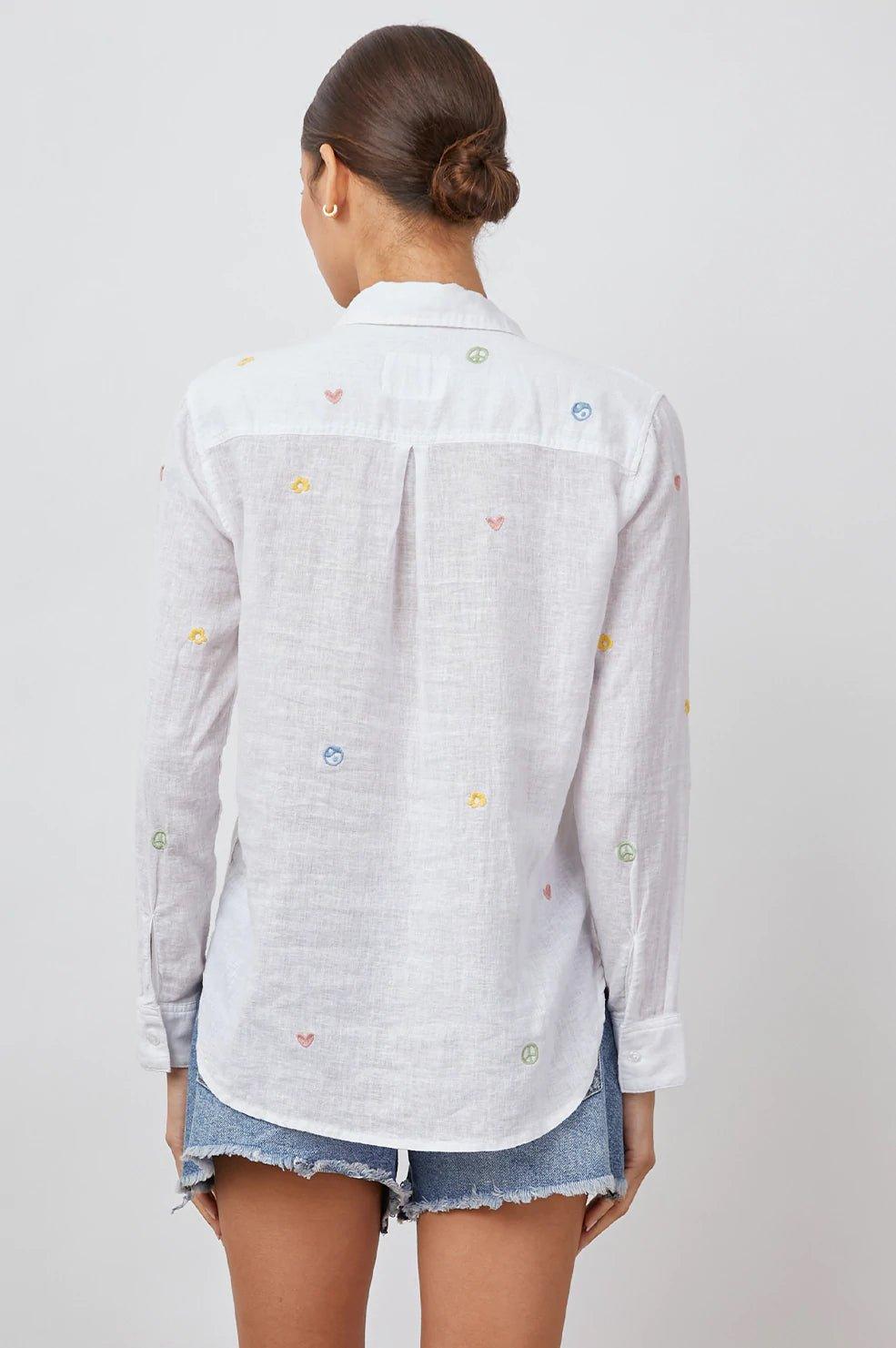 Dame med oppsatt hår iført hvit skjorte med brodert peace-tegn og hjerter, kombinert med olashorts.