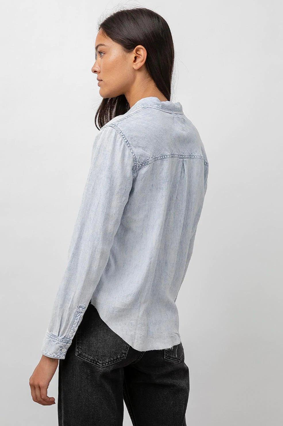 Kvinne i lys denimskjorte med syrevask, sett bakfra, svarte jeans, minimalistisk stil.