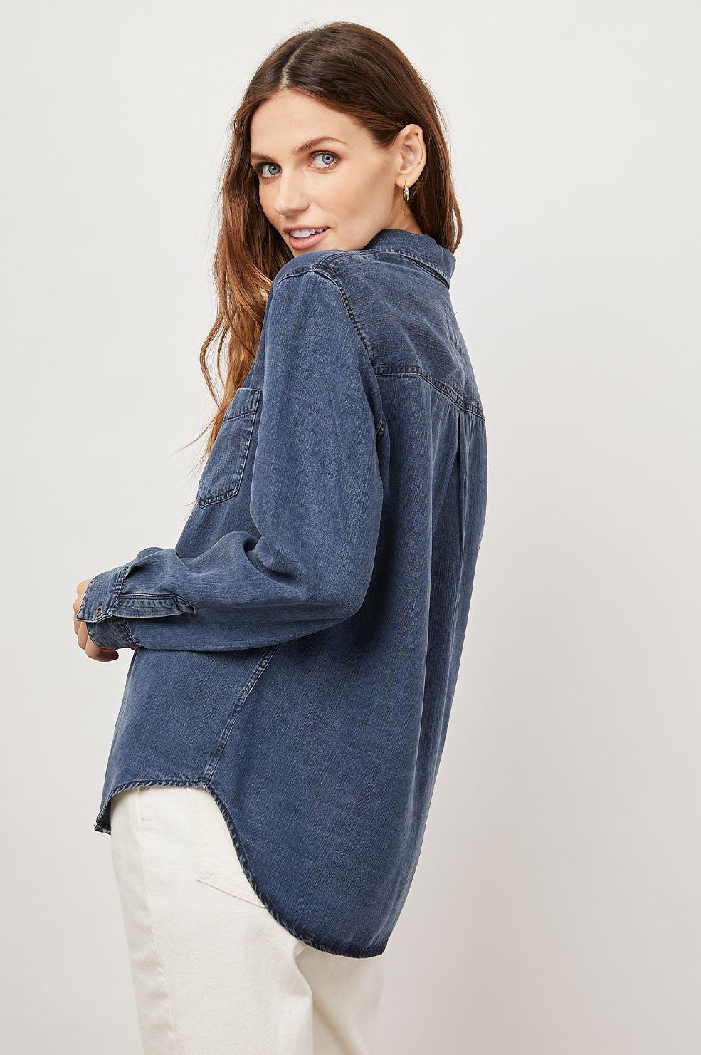 Dame i mørk denimskjorte og lyse bukser mot lys bakgrunn, moteriktig og avslappet stil