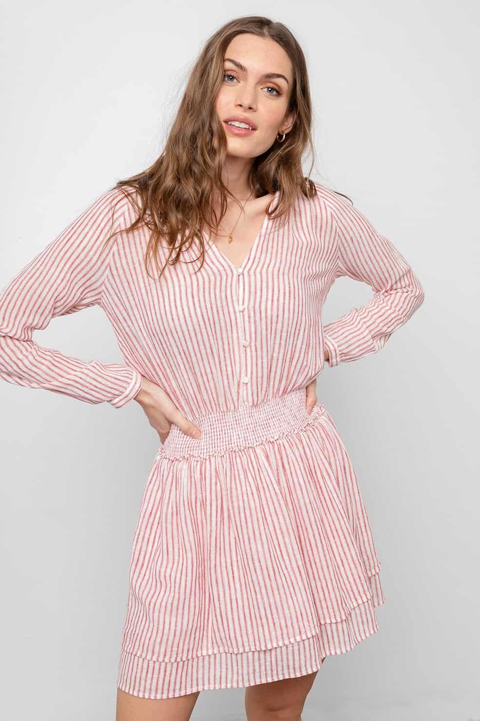 Kvinne i kort, langermet kjole med rosa og hvite striper, v-utringning og knapper.