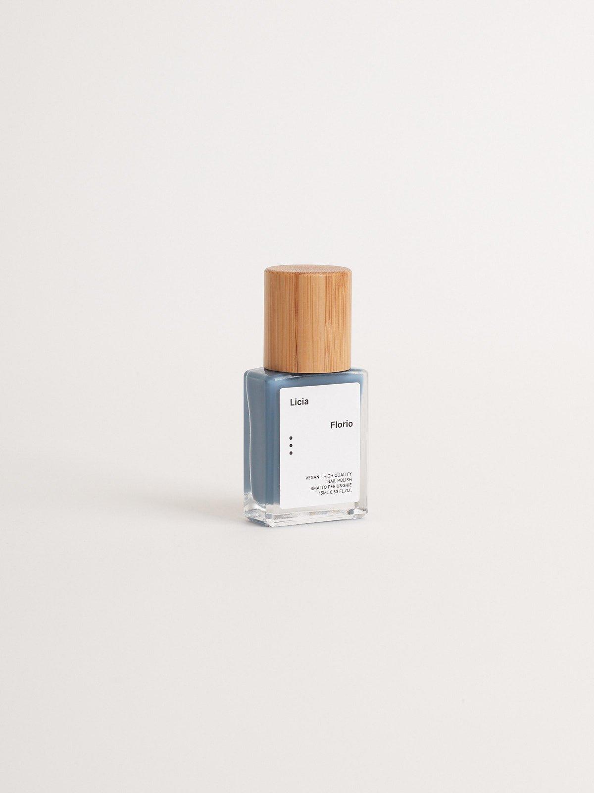 Blå neglelakkflaske med trelokk på lys bakgrunn, moderne og minimalistisk design.