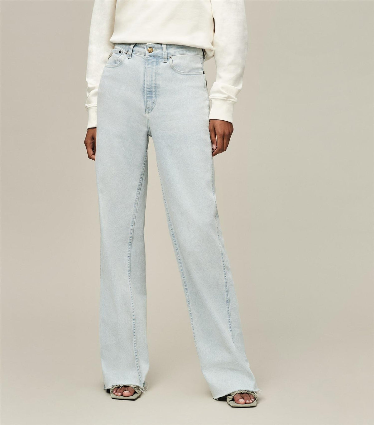 Dame med lyseblå vide jeans og hvit genser, mot enkel bakgrunn