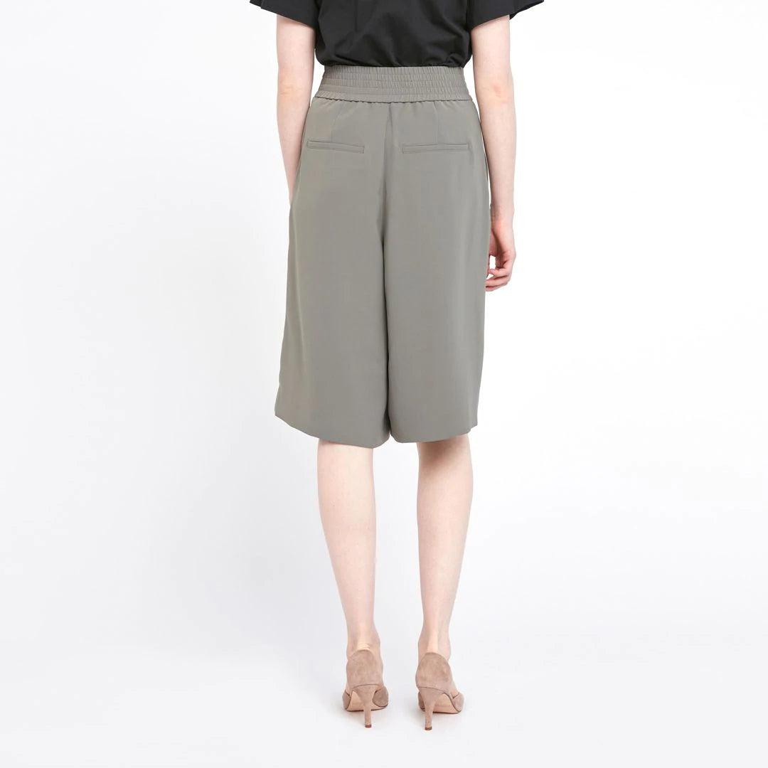 Dame i olivengrønne bermudashorts med høyt liv og vide ben, sett bakfra mot hvit bakgrunn.