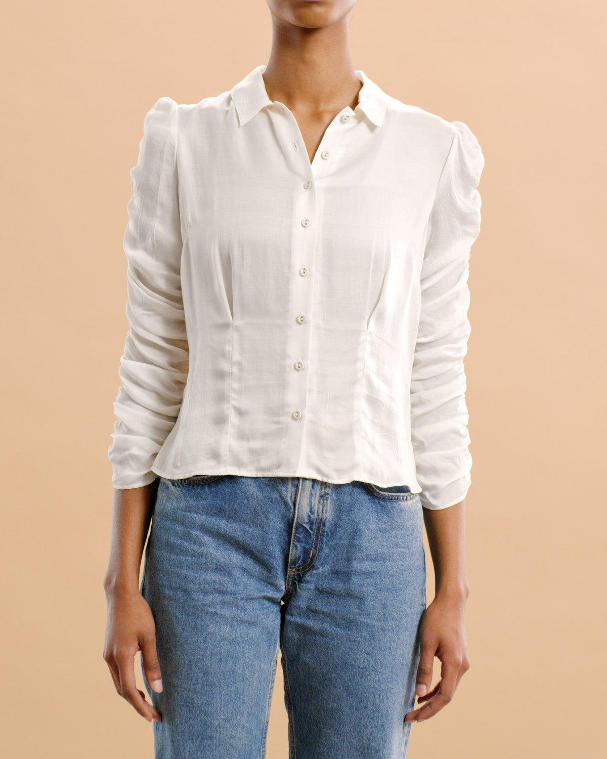 Dame i hvit satengskjorte med knapper og blå jeans mot beige bakgrunn