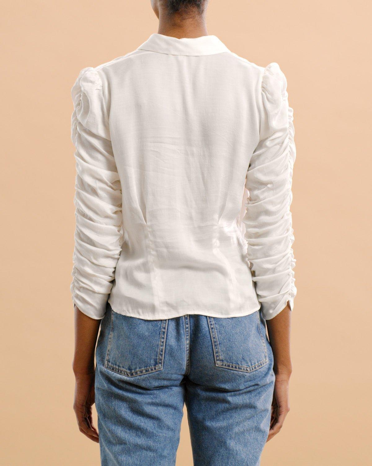 Kvinne med hvit satengskjorte med rynkede ermer og blå jeans, sett bakfra.