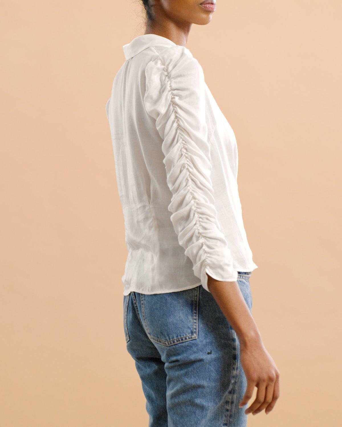 Kvinne med hvit satengskjorte med rynkede ermer og blå jeans, beige bakgrunn