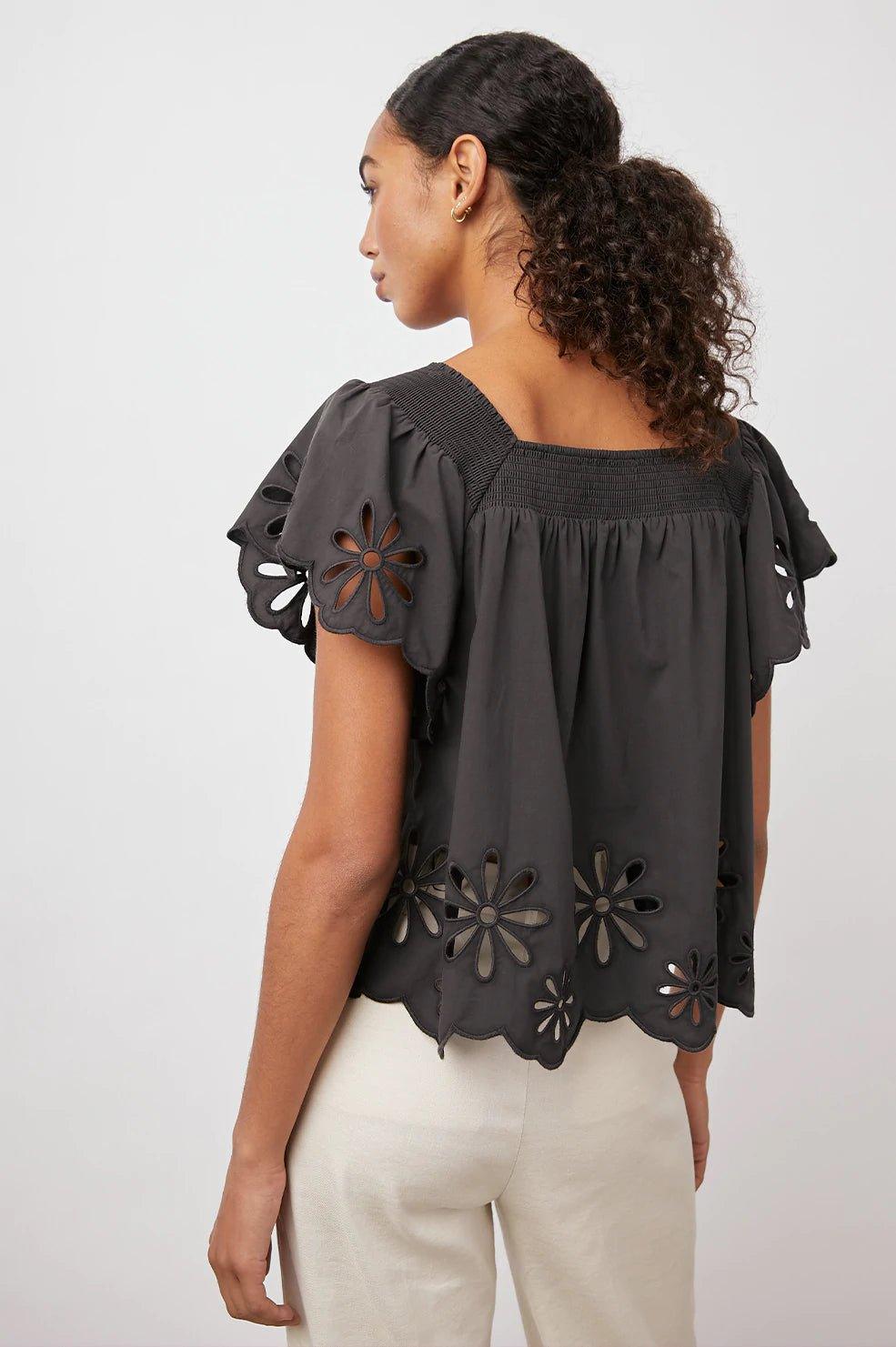 Kvinne med svart bluse med broderte blomsterdetaljer og korte ermer, sett bakfra