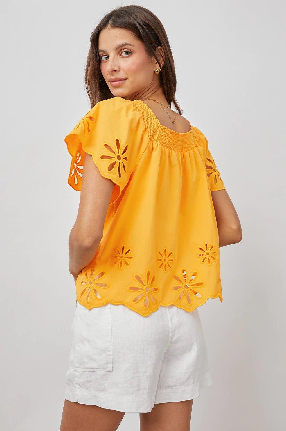 Kvinne i gul brodert bluse med blomsterdetaljer og hvite shorts, sommermote dame